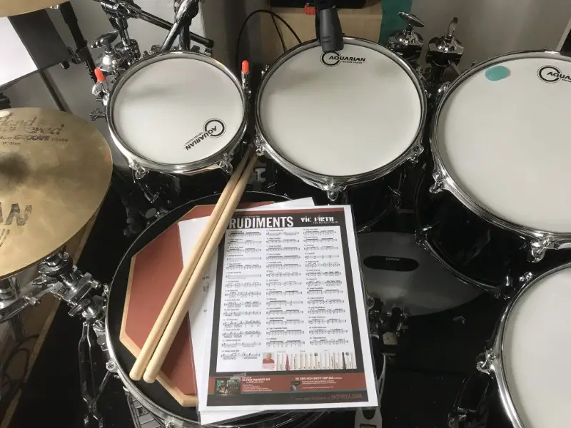 Drumsticks on a drum practice pad including drum rudiments on sheet music.